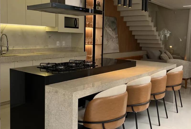 Cozinha planejada com ilha gourmet em pedra, banquetas em couro e iluminação embutida