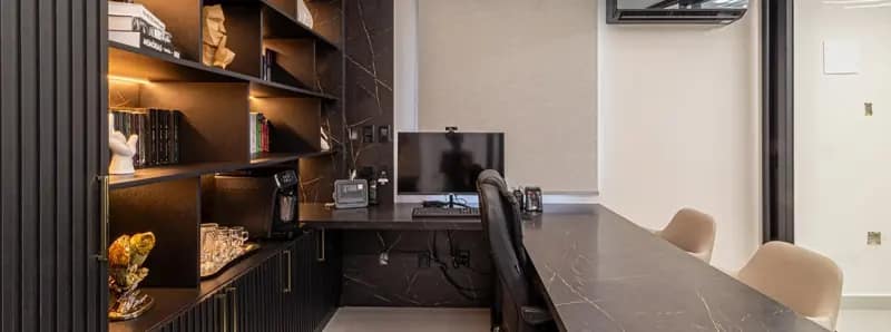 Home office com estante de nichos iluminados e bancada em pedra escura